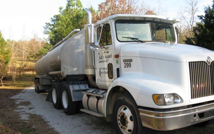 White tanker truck parked on a roadside near trees in autumn