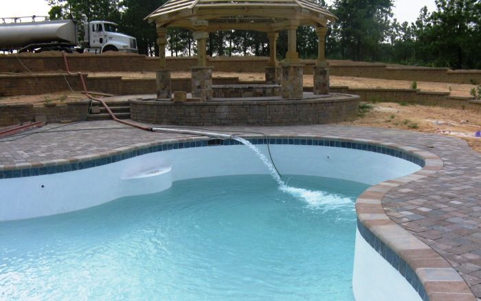 Backyard swimming pool with curved stone deck and a covered gazebo in the background