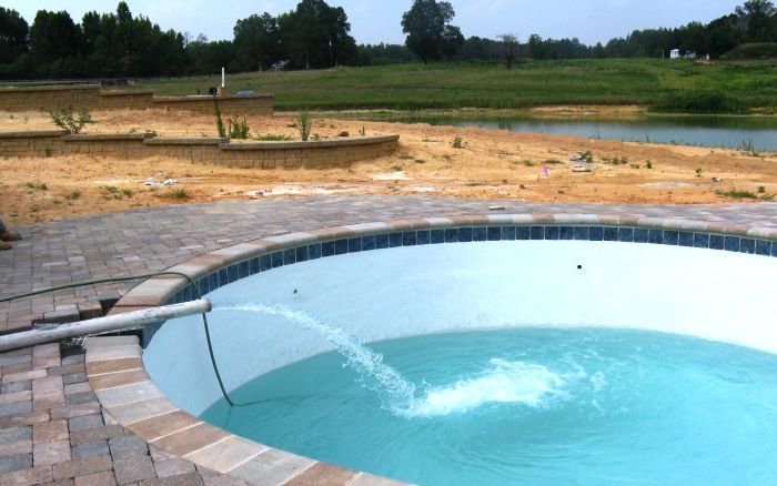 Backyard pool with a hose spraying water into a blue, empty basin under construction