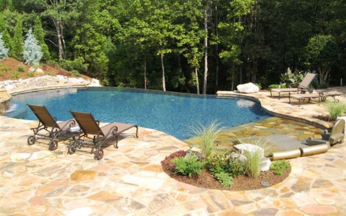 Backyard swimming pool with stone deck, lounge chairs, and lush green trees surrounding it