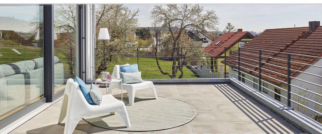 A balcony with chairs and a table with a view of a garden.