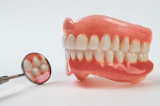 A set of complete dentures sits next to a small dental mirror on a white surface.