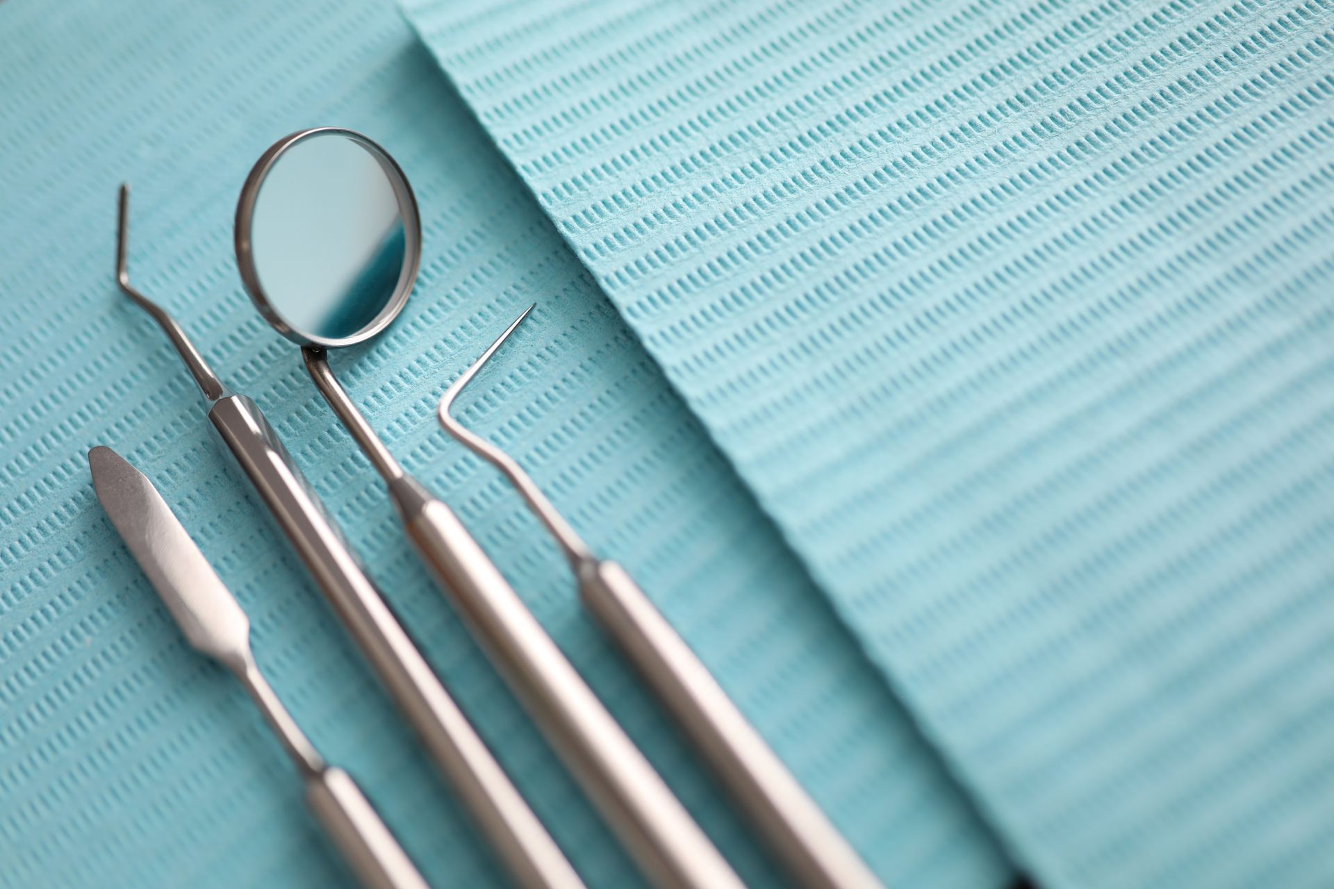 Dental tools including a mirror, explorer, and spatula arranged on a textured light blue medical bib. Dental tools including a mirror, explorer, and spatula arranged on a textured light blue medical bib.