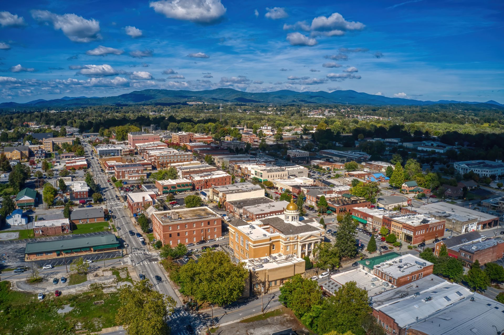 Aerial view of a small town with a central golden-domed building, surrounded by greenery and distant rolling mountains. Aerial view of a small town with a central golden-domed building, surrounded by greenery and distant rolling mountains.