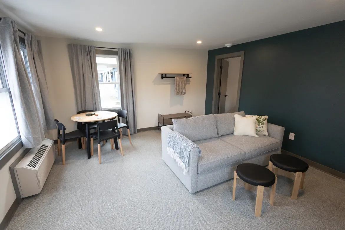 Modern living room with gray sofa, small tables, dining nook, and teal accent wall