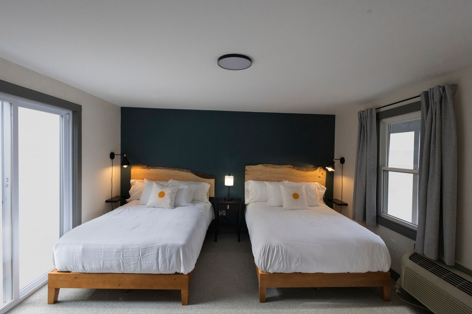 Modern bedroom with two twin beds, dark teal accent wall, and gray curtains.