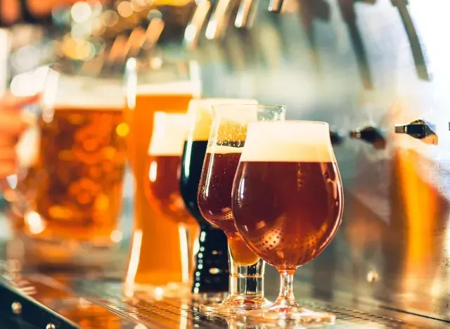 Row of amber craft beers in glasses on a bar counter, with foamy tops and warm lighting