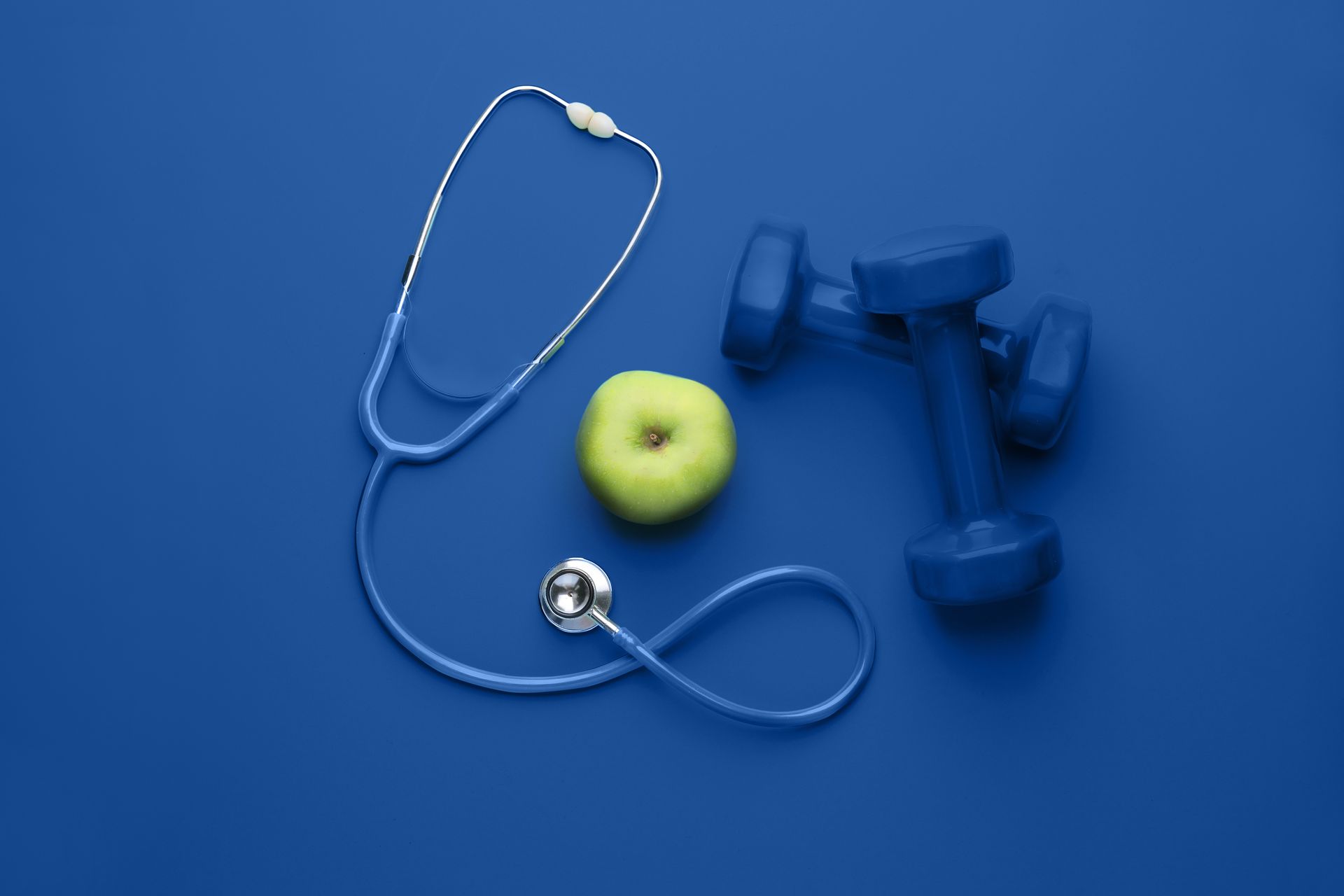 Weight Loss Services concept with an apple, dumbbells, and stethoscope on a blue background.