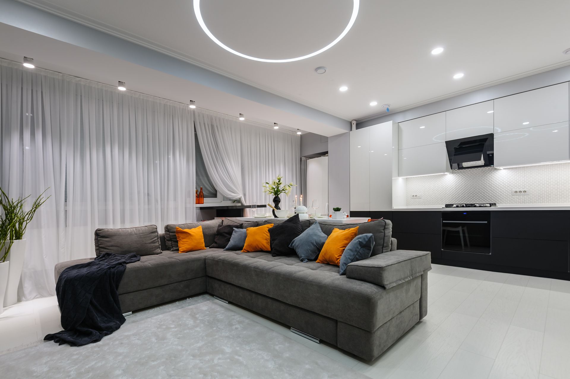 Modern gray sectional sofa with orange pillows in a bright contemporary living room and kitchen area