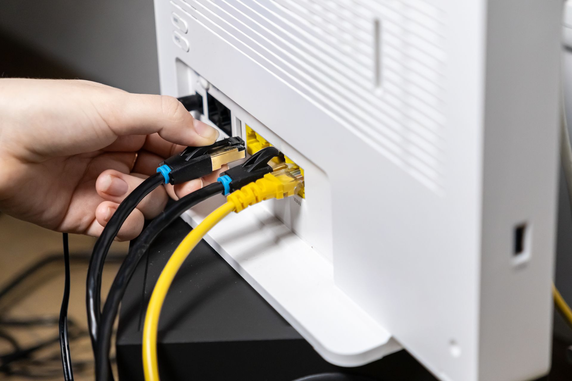 Hand plugging Ethernet cables into the back of a white router or modem