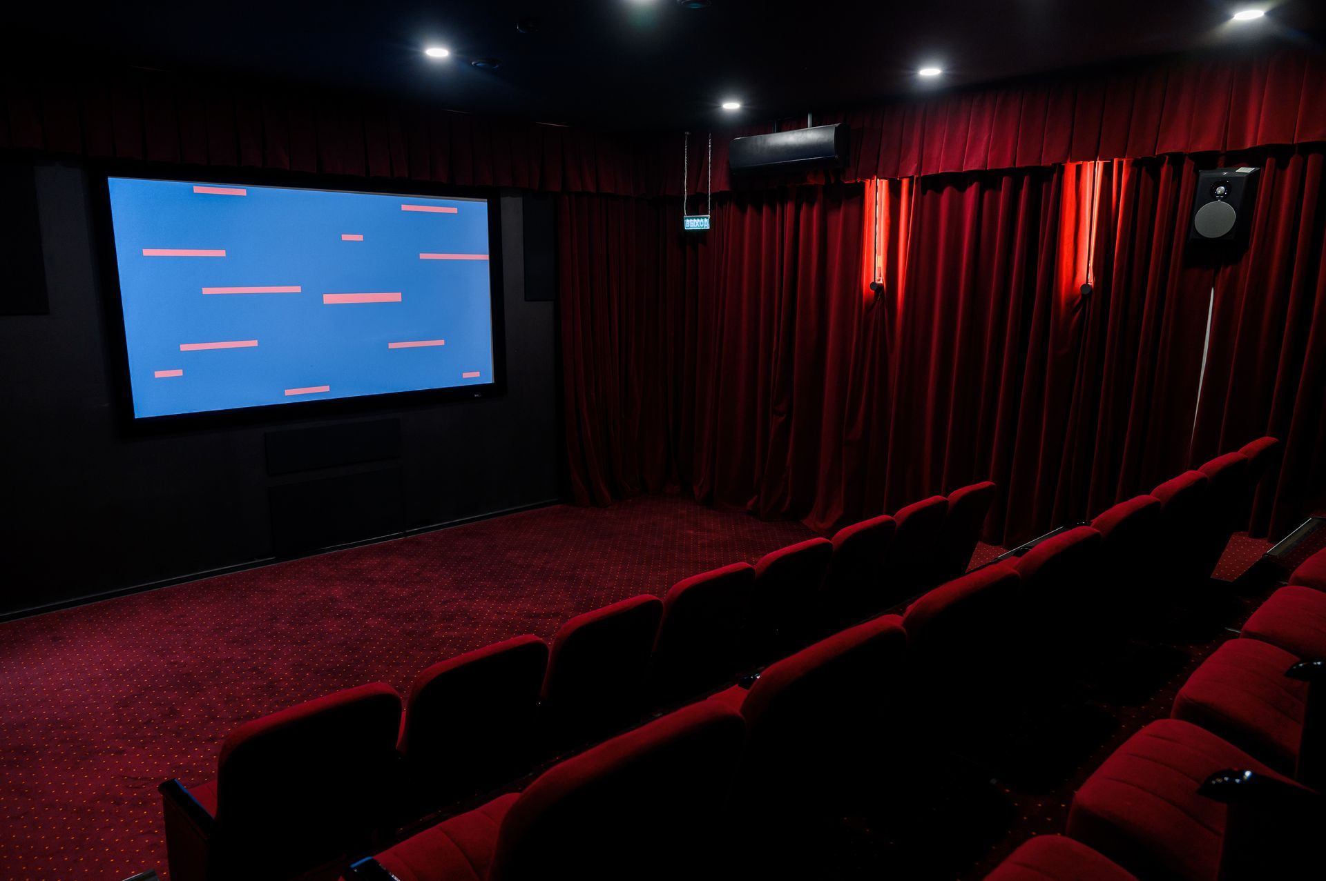 Empty cinema theater with red seats, dark curtains, and a blue screen at the front.