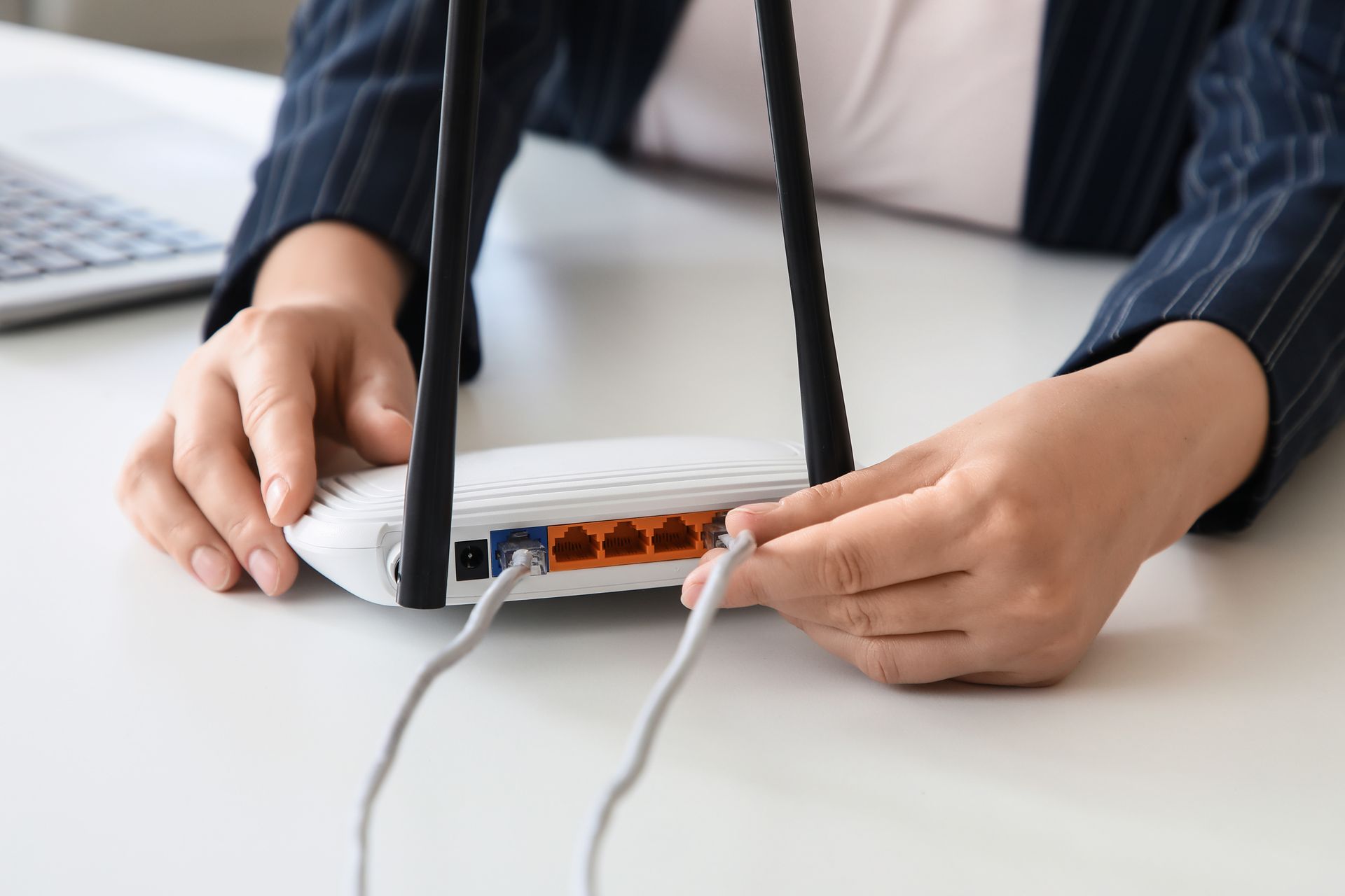 Hands connecting cables to a white Wi‑Fi router on a desk