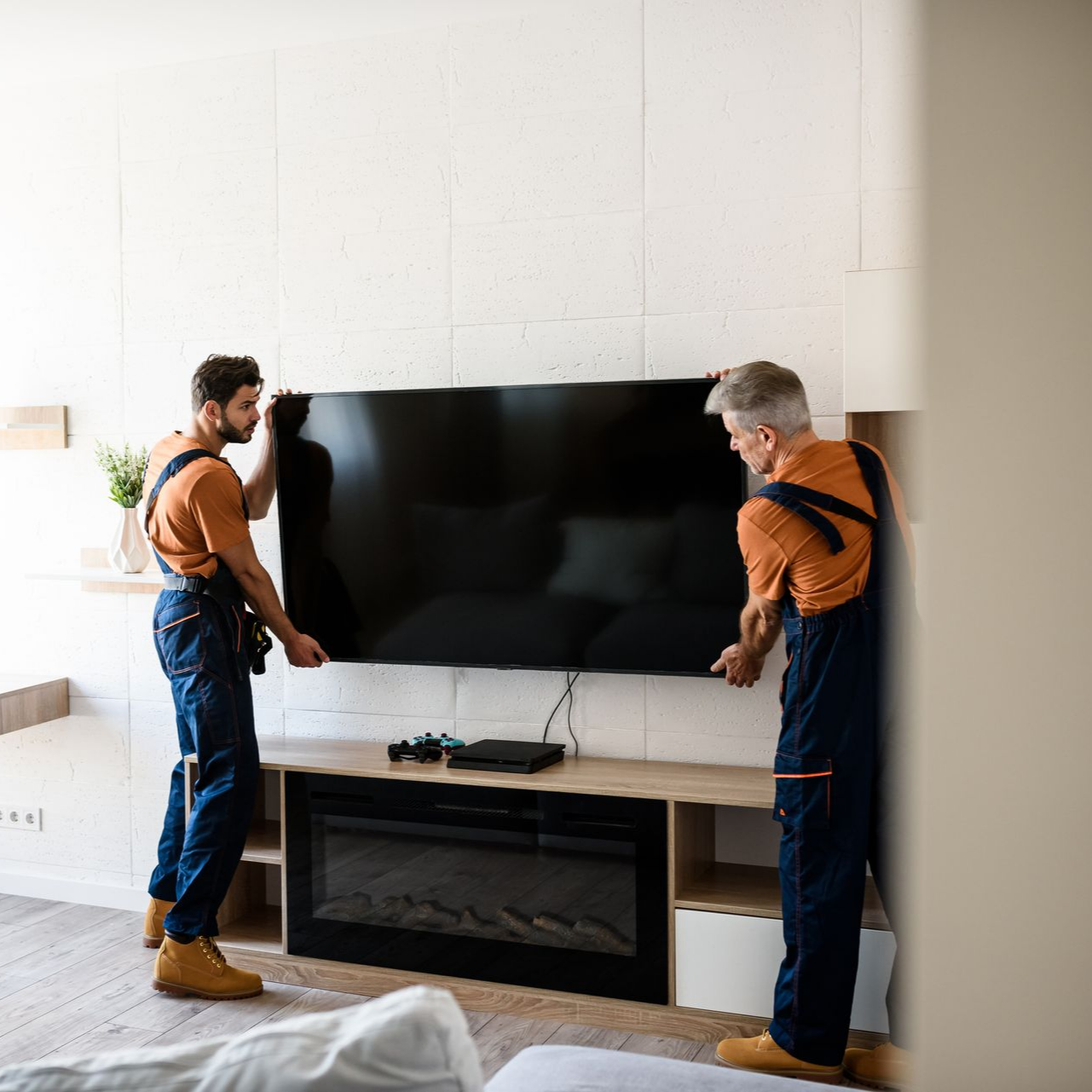 Two workers installing a large TV above a fireplace in a bright living room