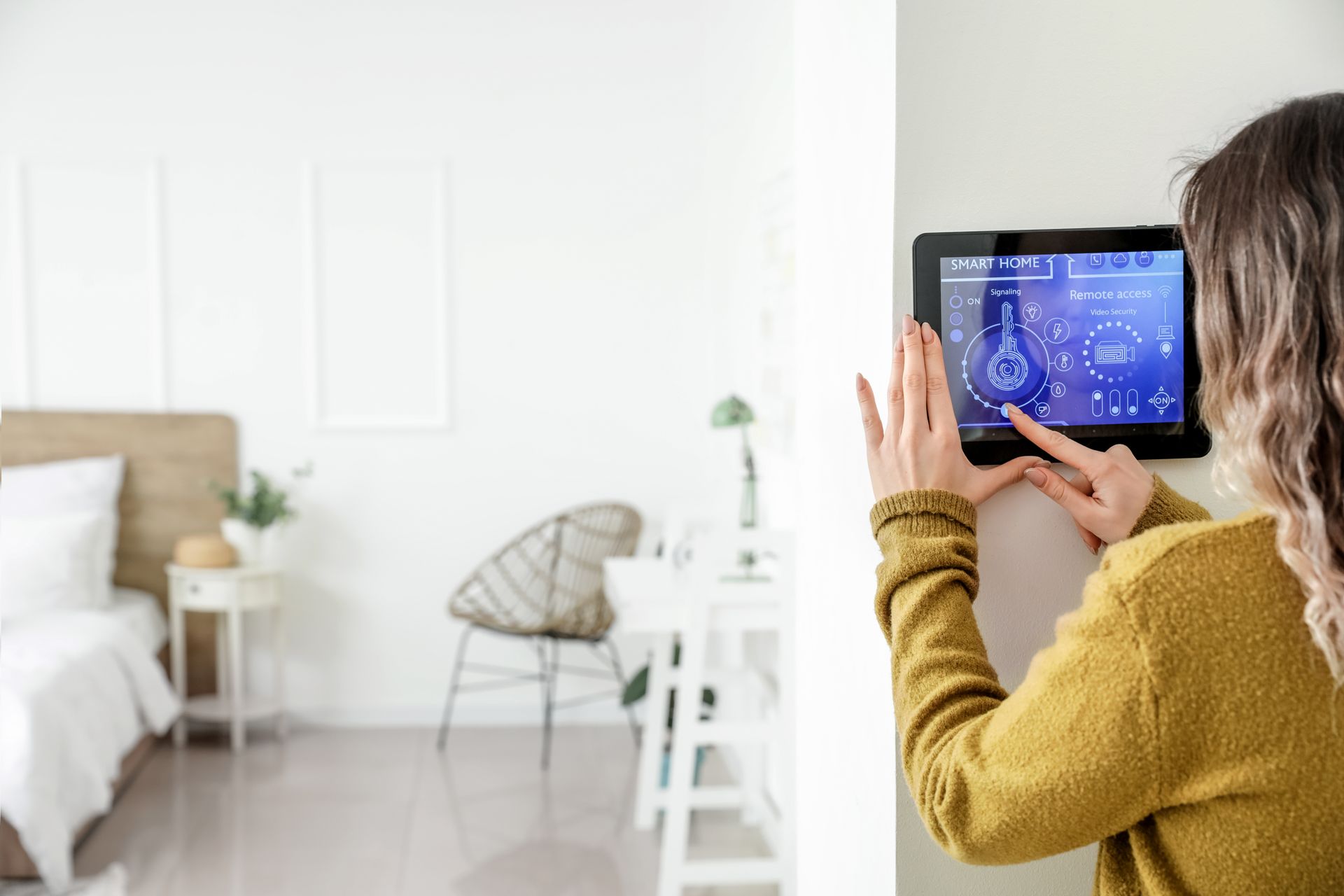 Person using a wall-mounted tablet in a bright bedroom, adjusting a smart home control panel