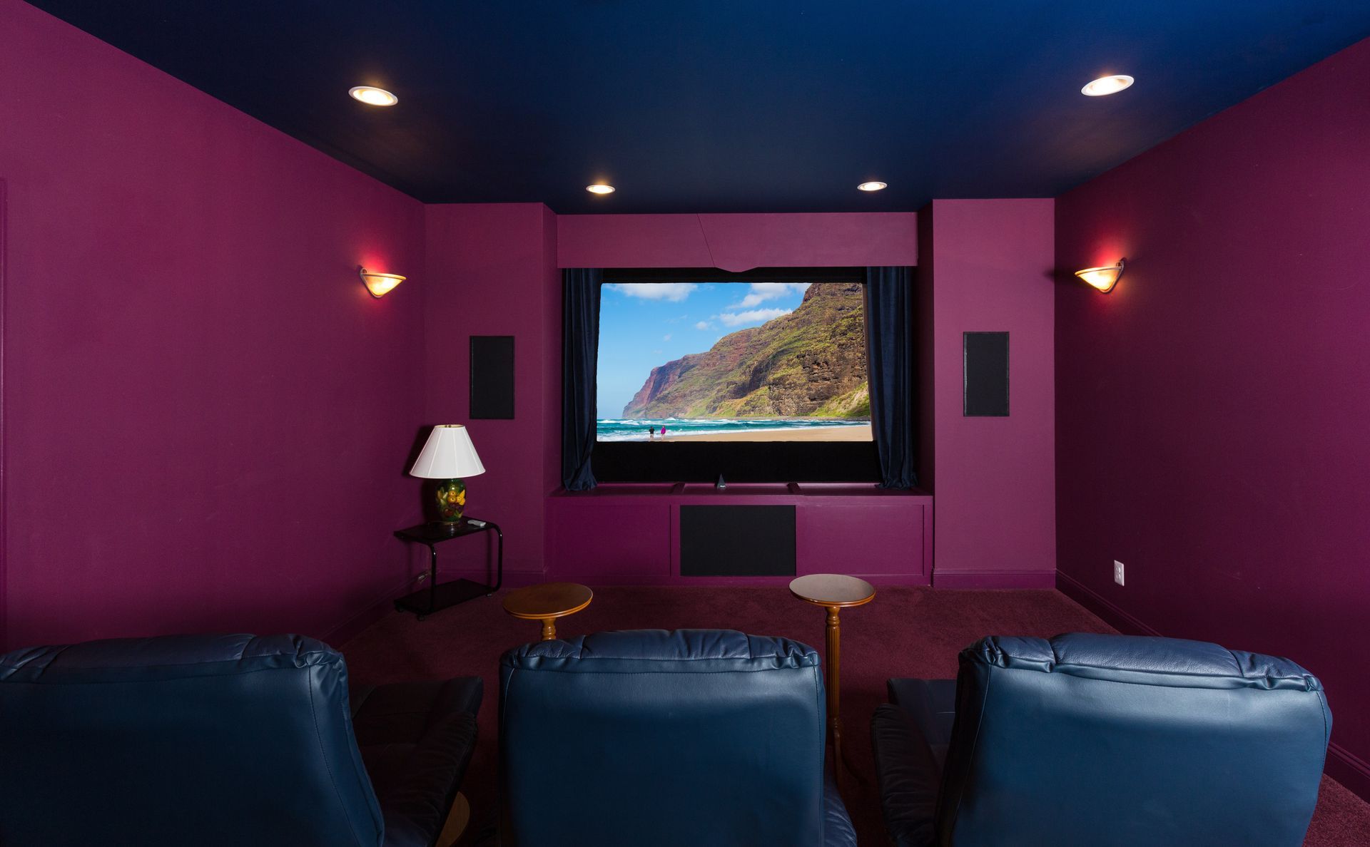 Purple home theater room with blue recliners facing a wall-mounted TV and soft lamps.