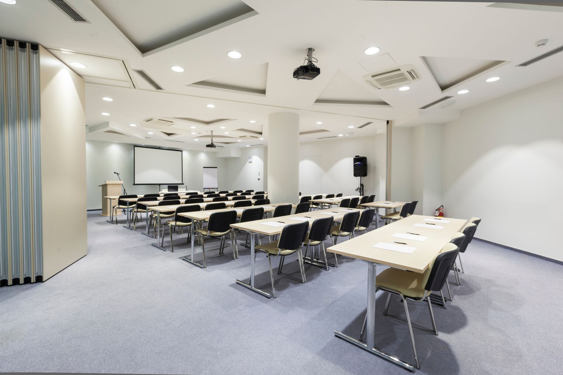 Empty conference room with rows of tables and black chairs under bright ceiling lights
