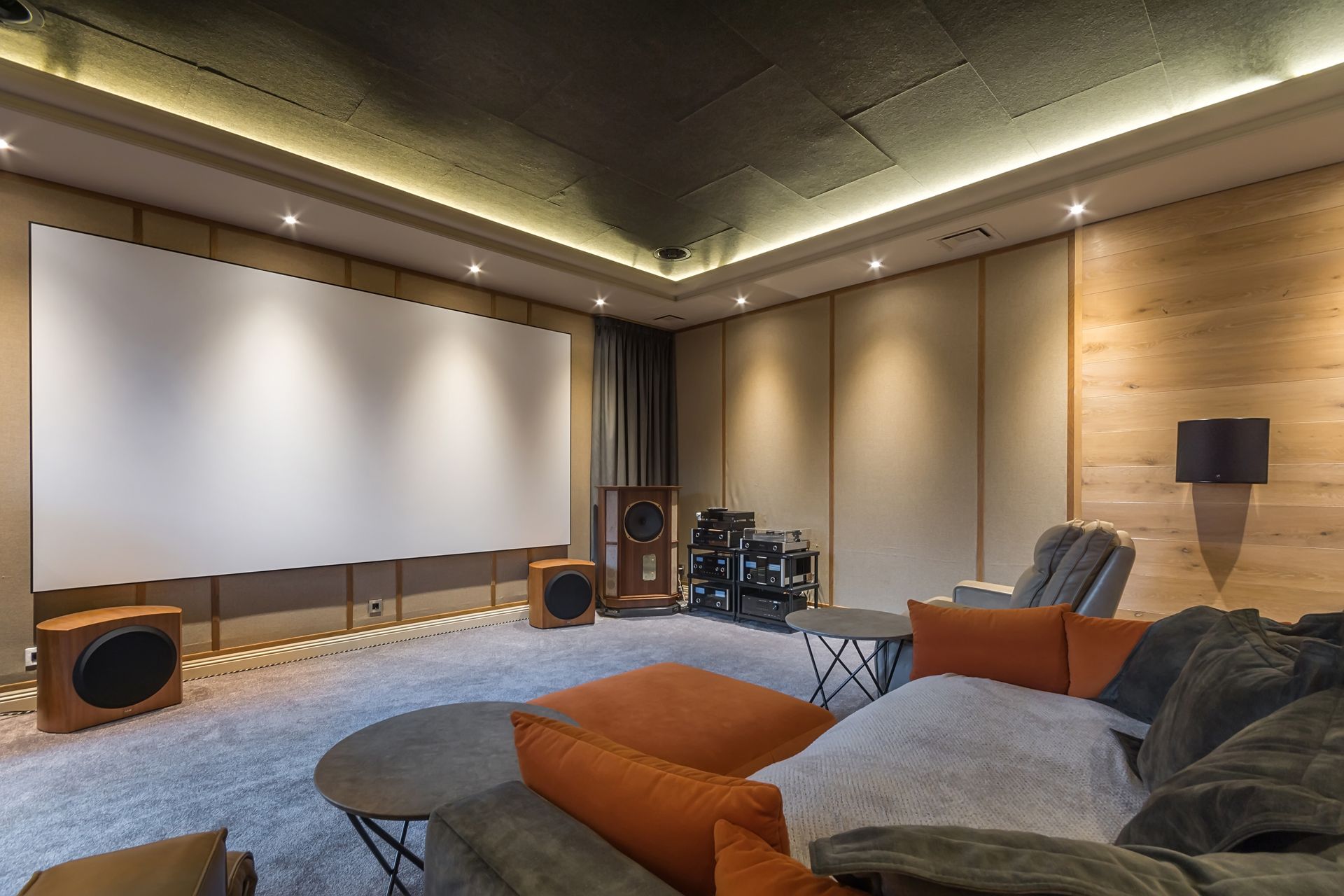 Modern home theater room with a large projector screen, speakers, and plush sectional seating