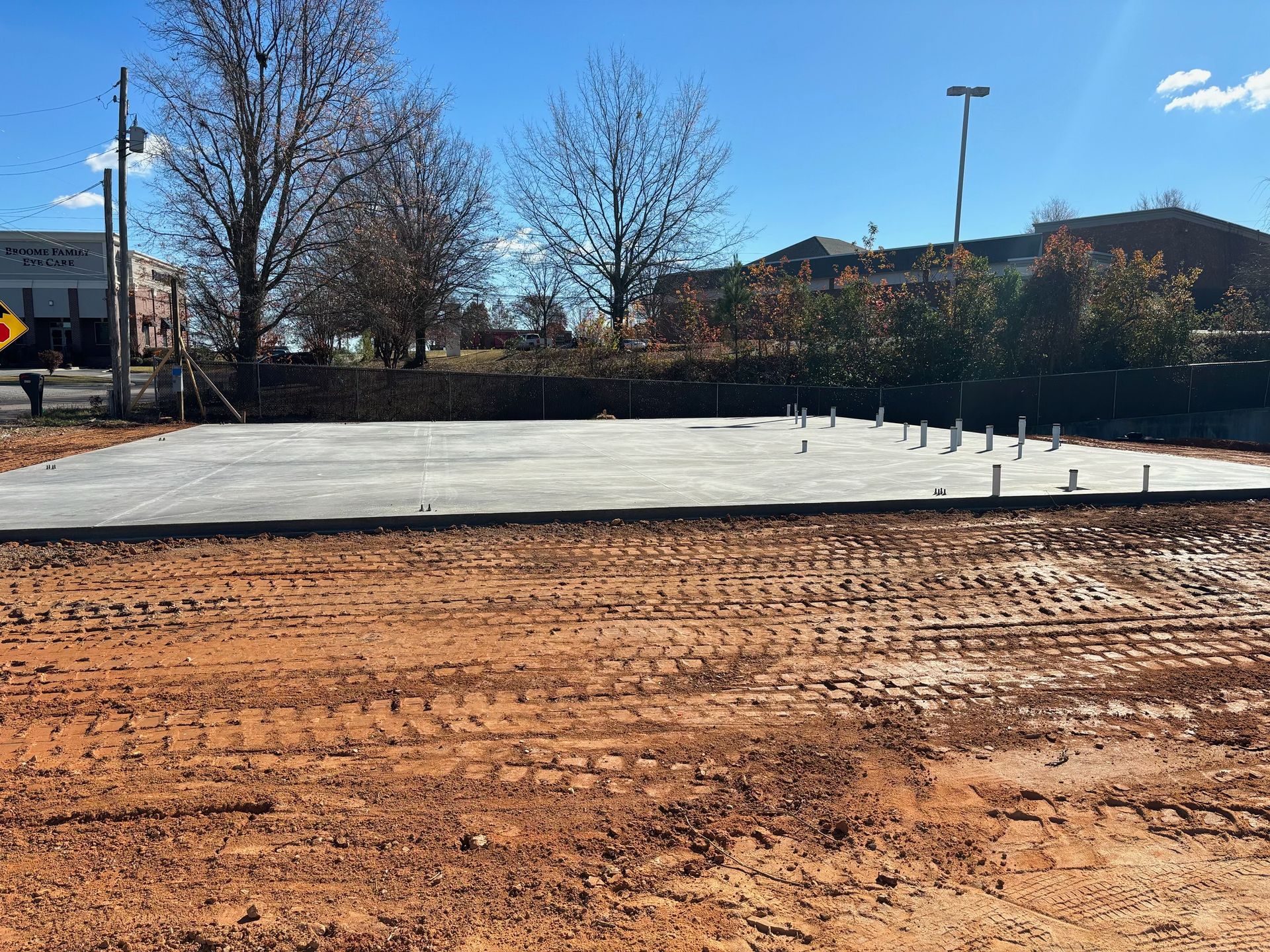 Construction site with a concrete foundation, bare trees, and brown soil in daylight.