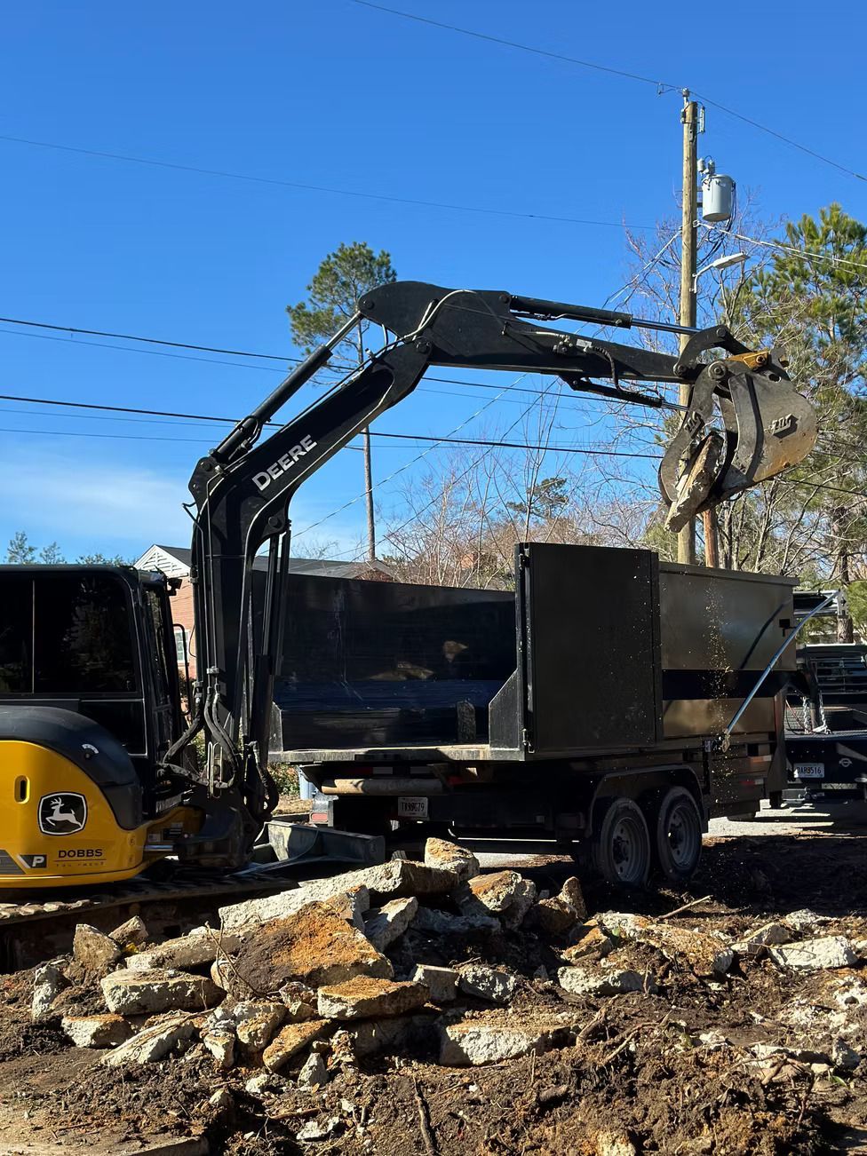 Excavator loading debris into a trailer on a construction site under a blue sky.
