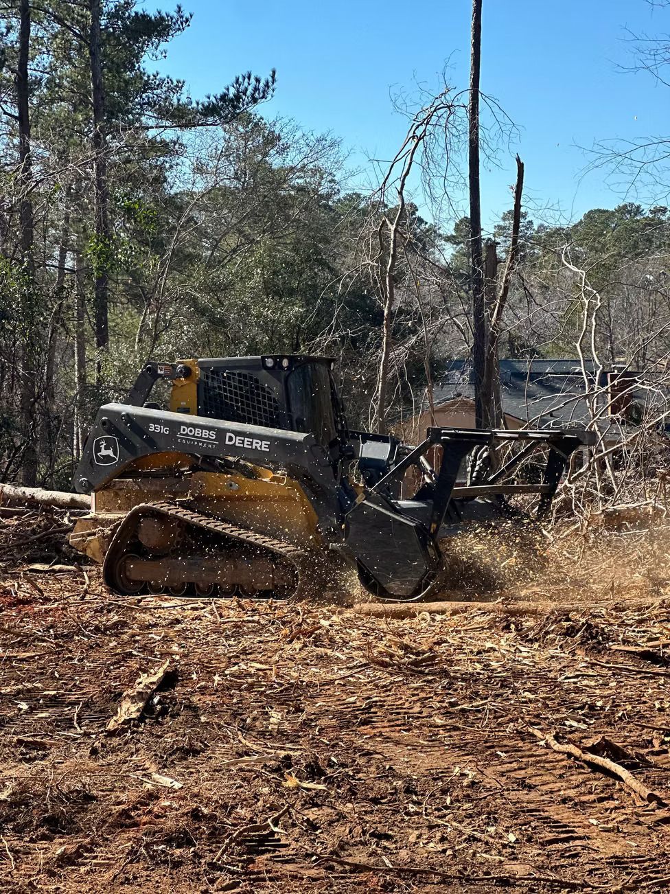 A yellow and black skid steer mulching wood on a sunny day.