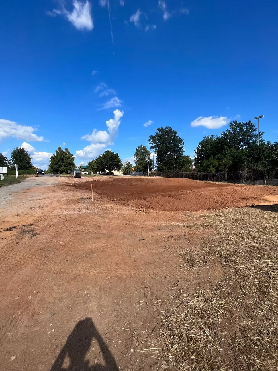 A large, cleared area of reddish-brown dirt under a bright blue sky, with trees in the background.