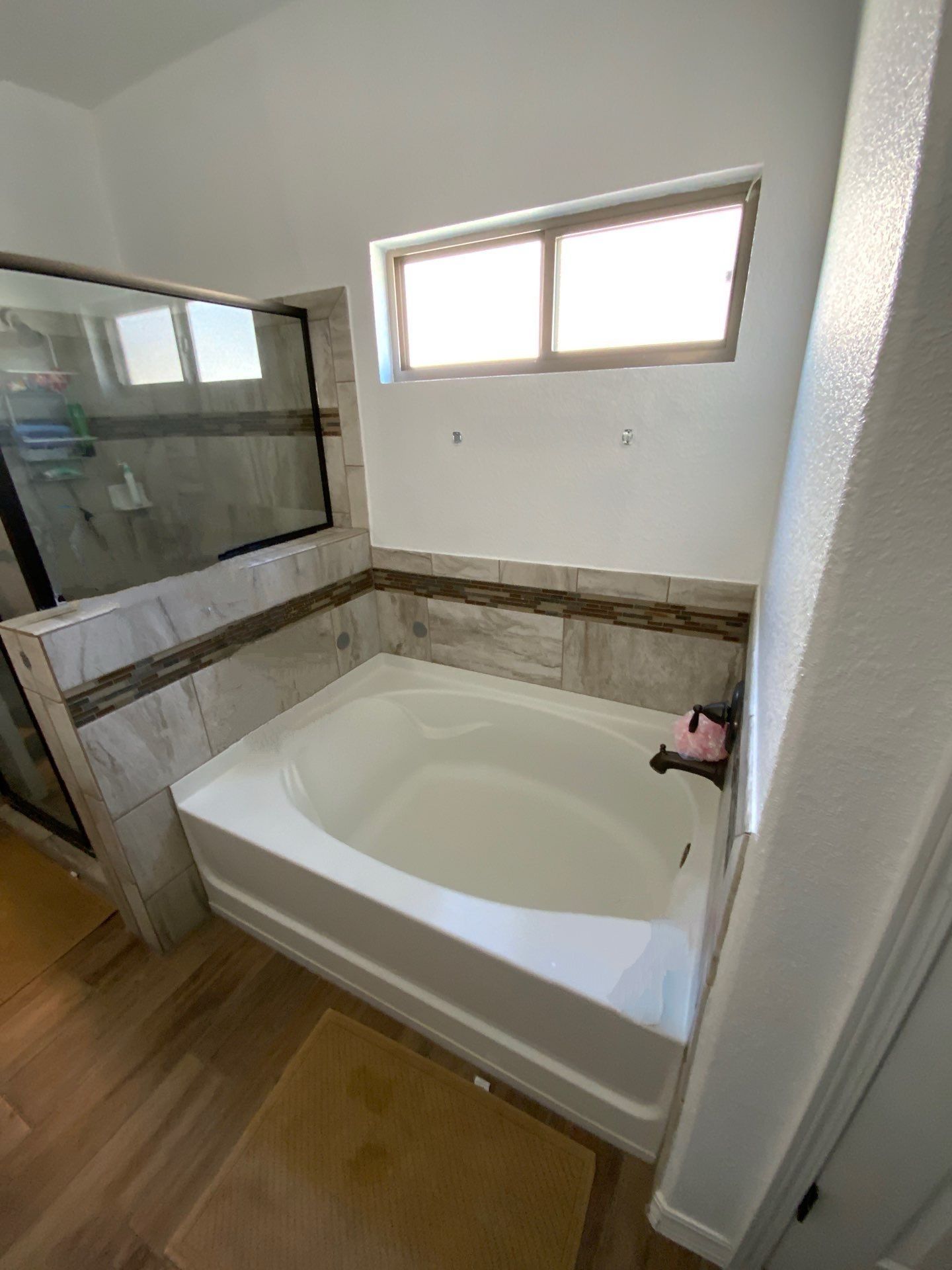 Bathroom with a white bathtub and glass shower door, light brown tiles.