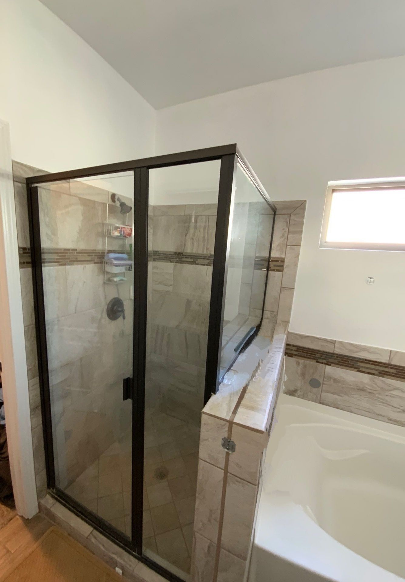 Shower stall with dark-framed glass door, tiled walls, and built-in tub alongside.