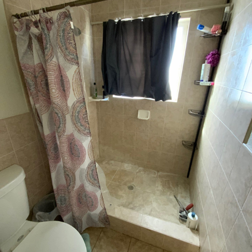 Bathroom with a shower stall, toilet, and curtain. Neutral tile, black shower curtain, and a pink and gray shower curtain.
