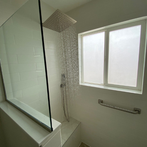 Shower with glass enclosure, rain shower head, frosted window, and grab bar.