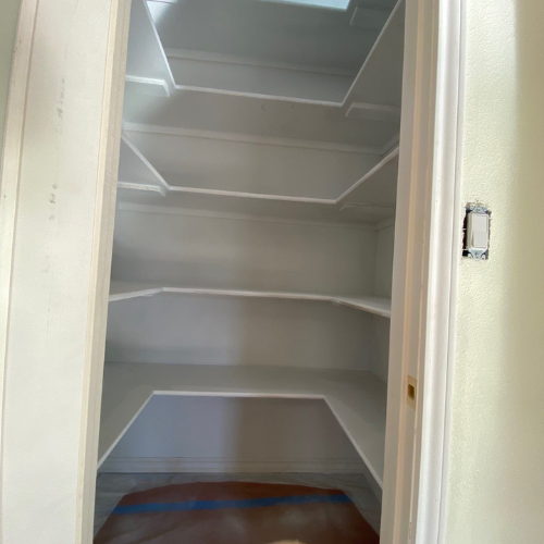 White-painted pantry with multiple shelves. Light switch is visible on the wall.