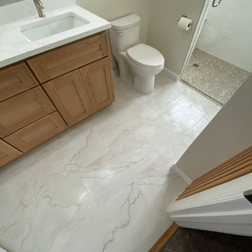 Bathroom with white marble-look floor and walls, wooden vanity, and shower.