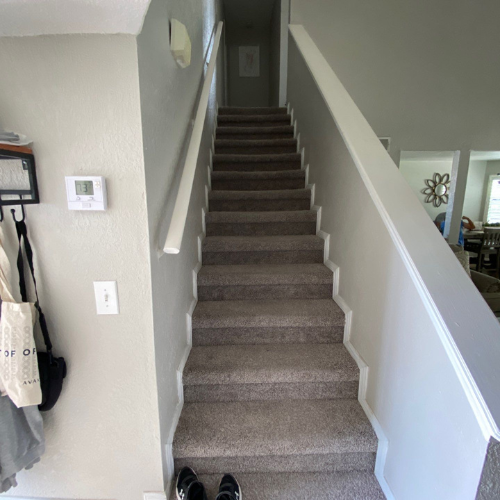 Staircase with carpeted steps leading upward; white handrails and gray walls; shoes at the bottom.