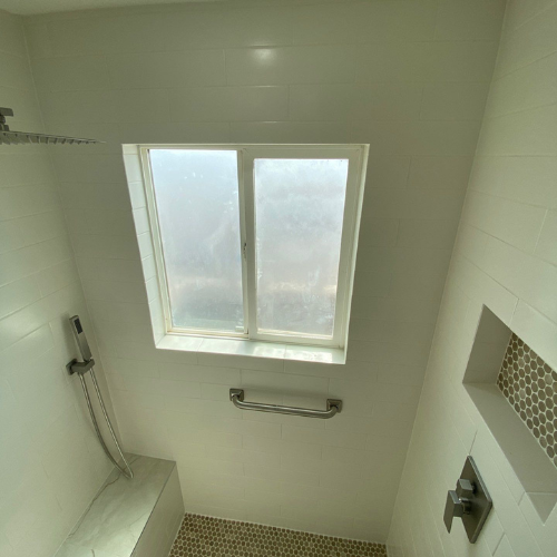 White tiled shower with window, bench, grab bar, and recessed shelf.