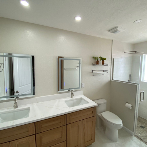 Modern bathroom with double sinks, toilet, and glass shower.