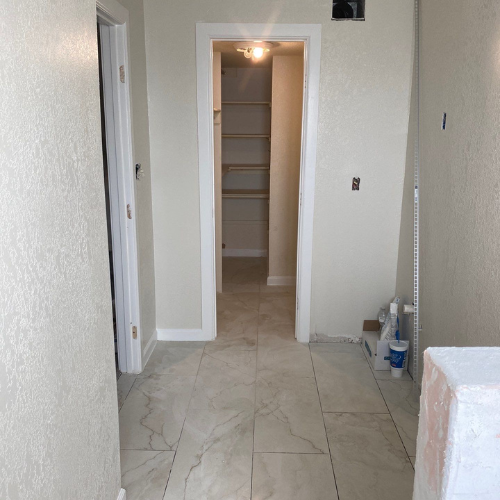 Hallway with off-white walls, tiled floor, and a closet at the end. An open door is visible on the left.