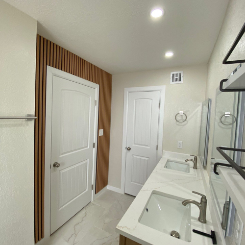 Bathroom with white walls, wood accent wall, double sink vanity, and white doors.