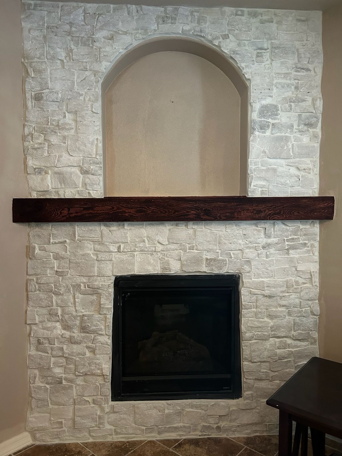 Fireplace with stone facade, arched alcove, and dark wood mantel.