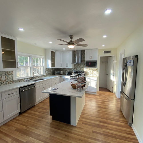 Newly renovated kitchen with white cabinets, island, stainless steel appliances, and wood flooring.