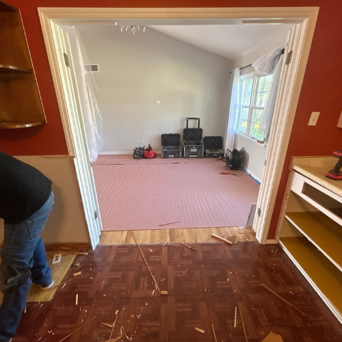 A doorway with a person working on the flooring. The room has pink underlayment.