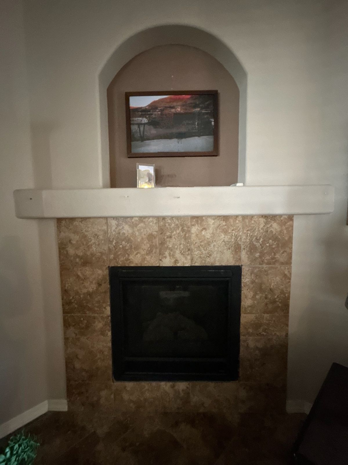 Fireplace with tiled surround, wooden mantle, and art in an arched niche above.