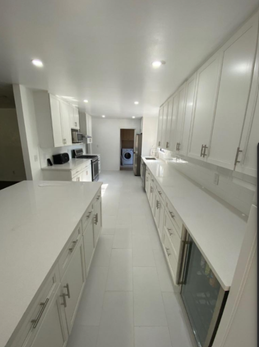 Bright white galley kitchen with long counters, cabinets, and recessed ceiling lights