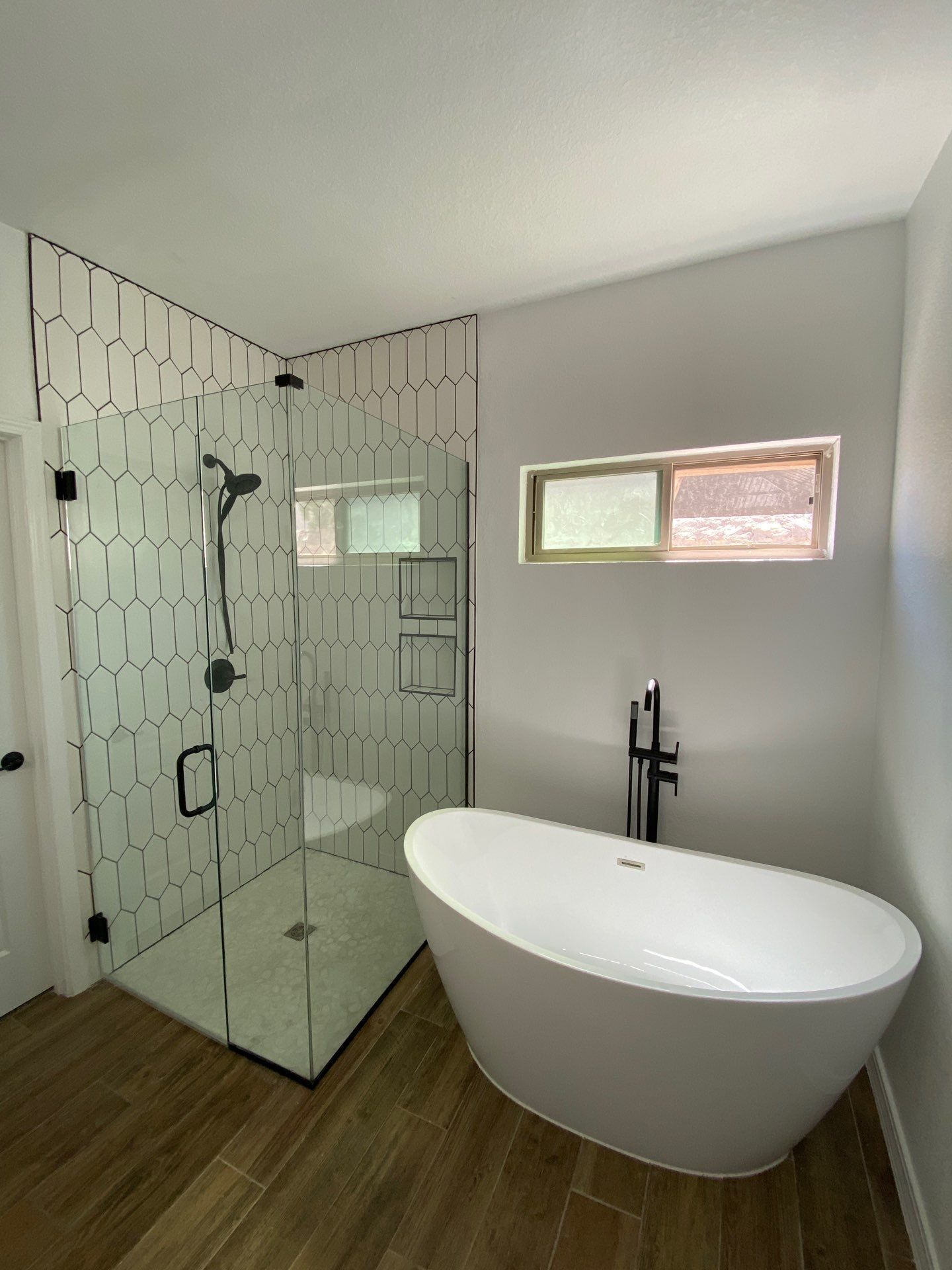 Modern bathroom with a white freestanding tub and a glass shower with black fixtures.