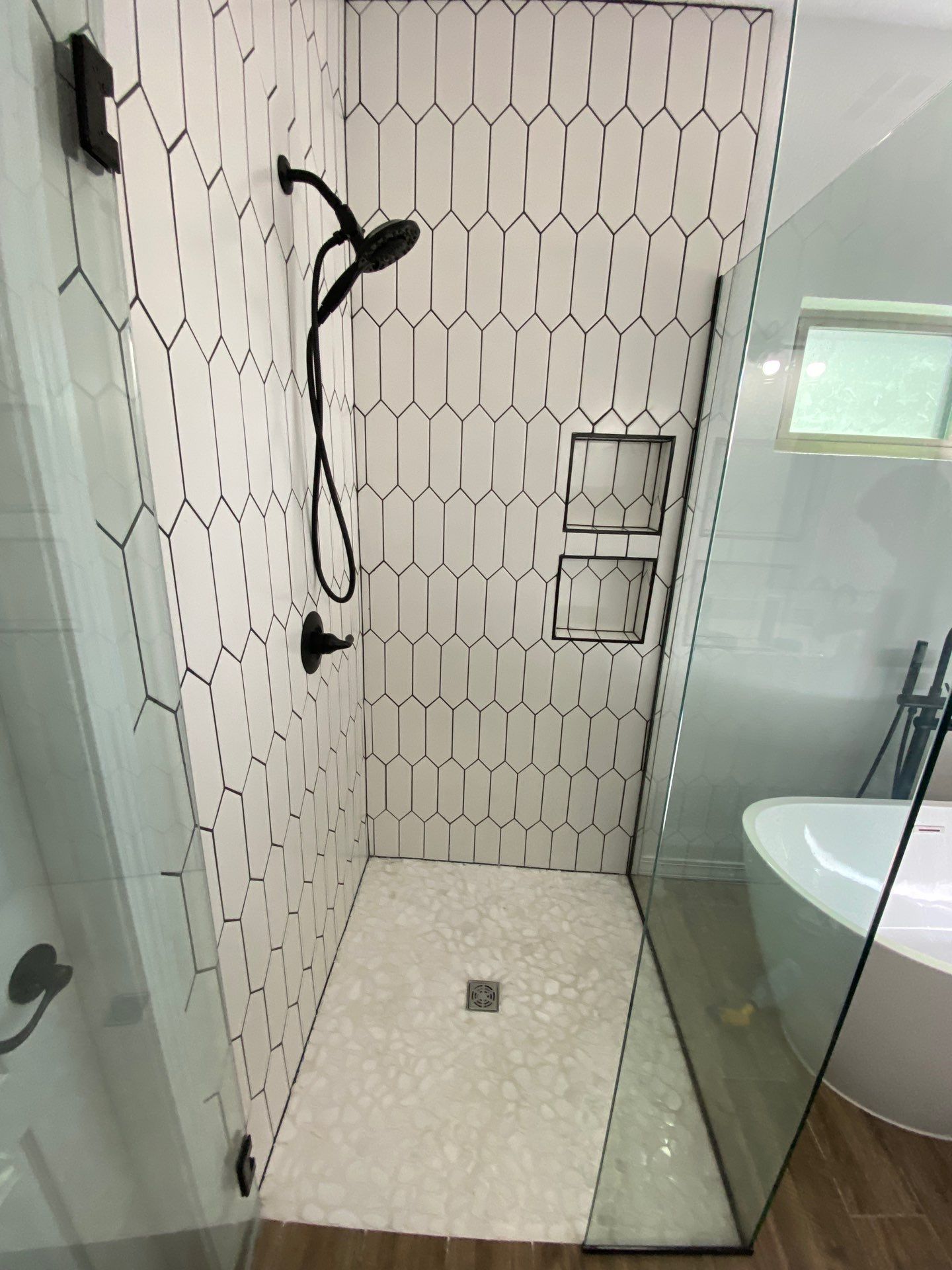 Shower with white and black tile, black shower fixtures, and glass doors.