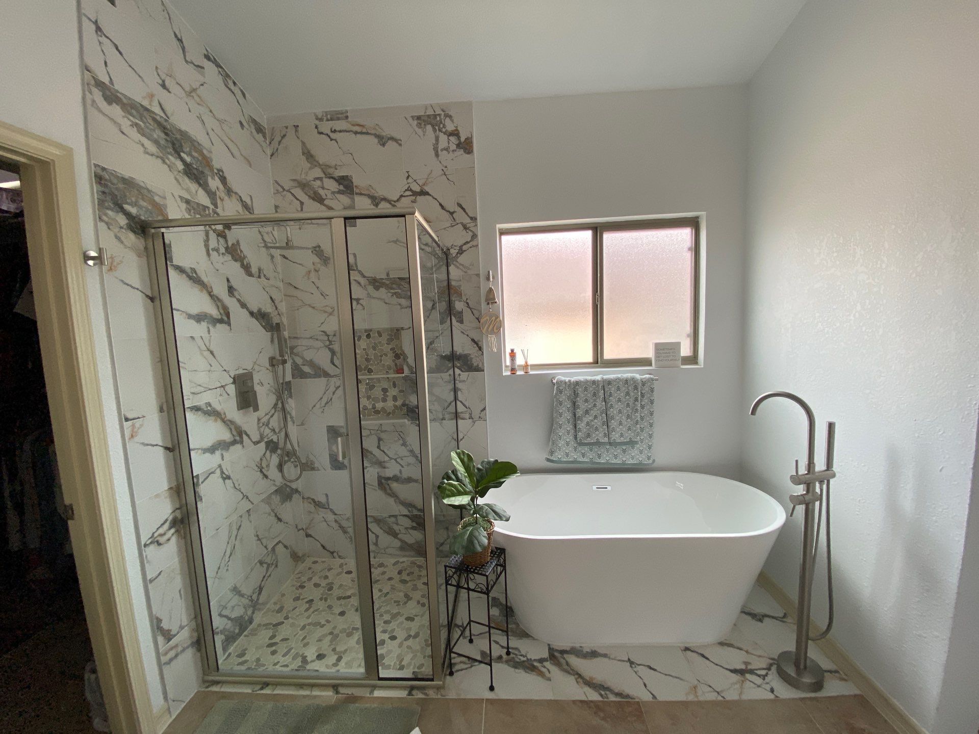 Bathroom with marble-look tile, glass shower, freestanding tub, and window.