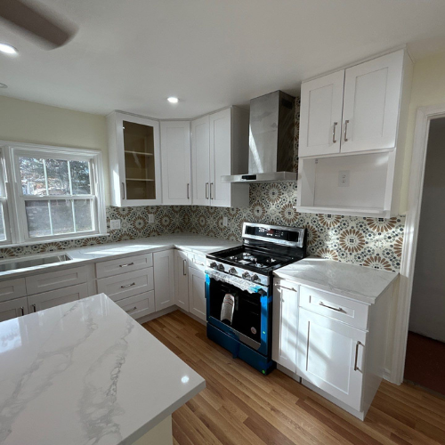 Bright kitchen with white cabinets, marble countertops, blue oven, and patterned backsplash.