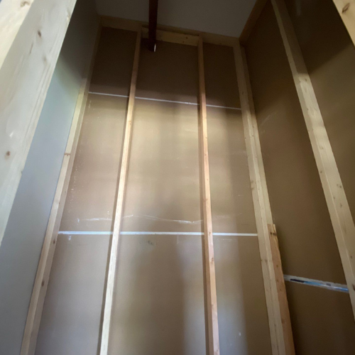 Interior unfinished closet with wooden studs and brown backing.
