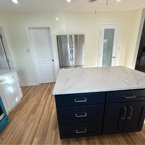 Kitchen with blue island, white countertops, stainless steel fridge, light wood floors, and white walls.