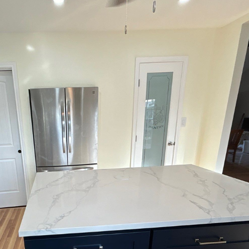 Kitchen with island, stainless steel refrigerator, white and blue countertop, and glass-paned pantry door.