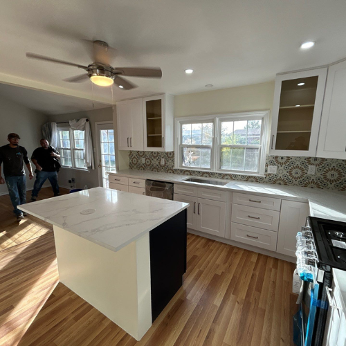 Newly renovated kitchen with white cabinets, island, and two people in the background.