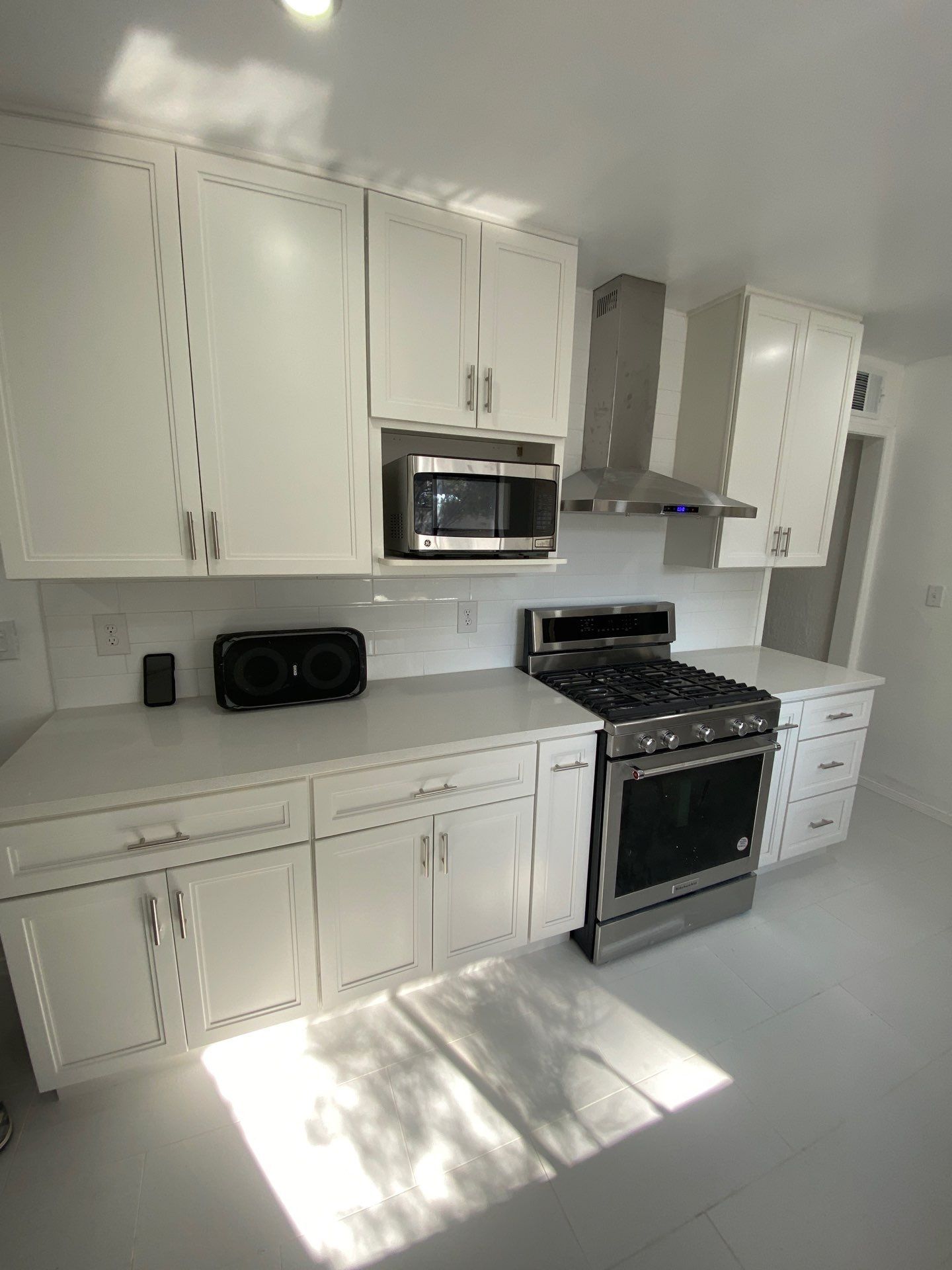 Bright white kitchen with cabinets, stove, microwave, and sunlight on the floor